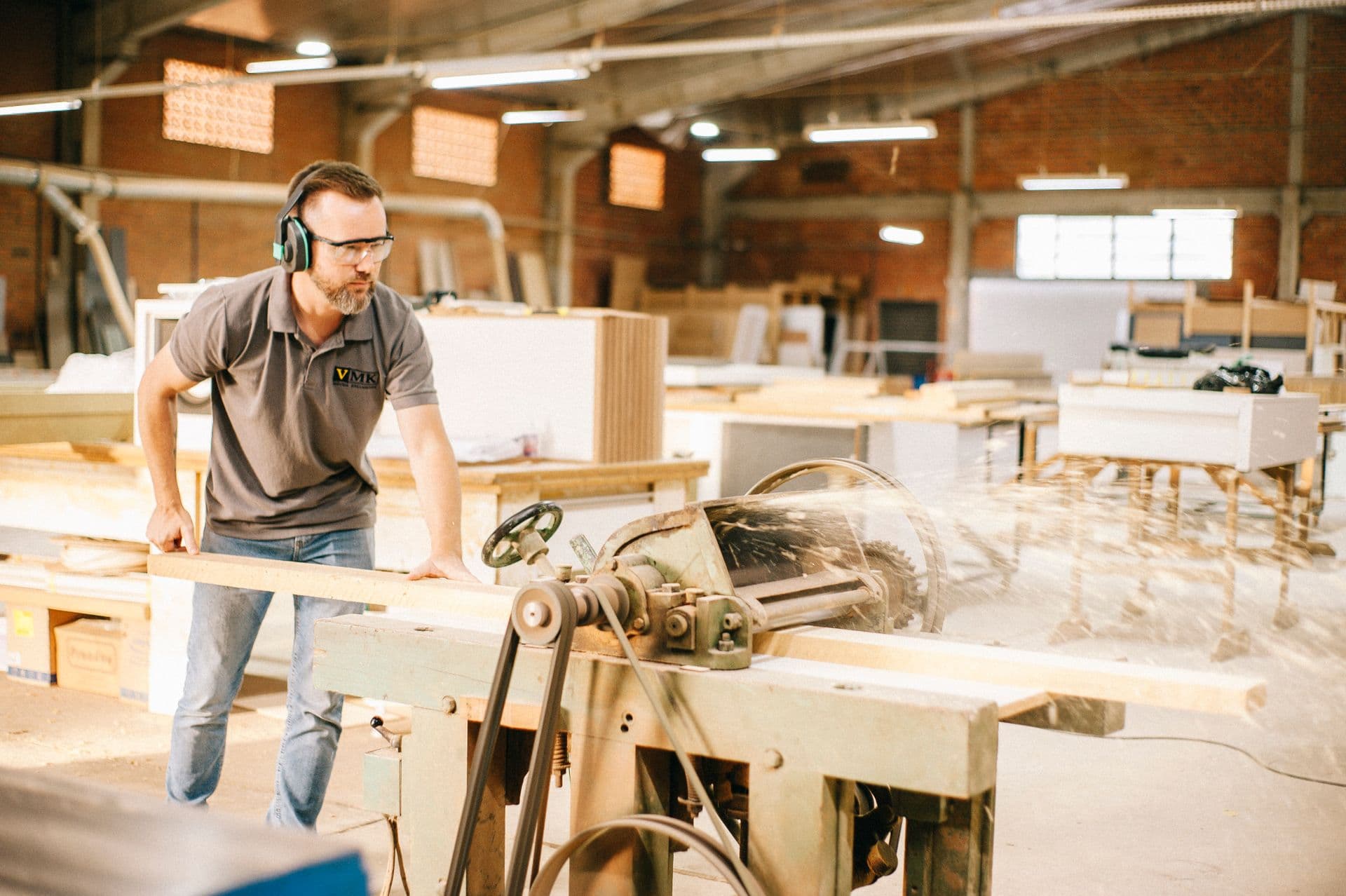 A carpenter at work on a saw bench in a busy workshop